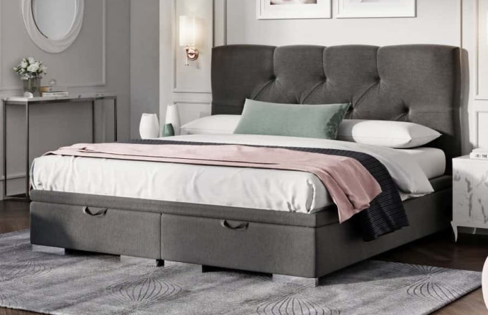 Eleganckie łóżko tapicerowane Lazio Maxi w ciemnoszarym kolorze z pikowanym wezgłowiem i pojemnikiem na pościel, w jasnej, klasycznej sypialni.